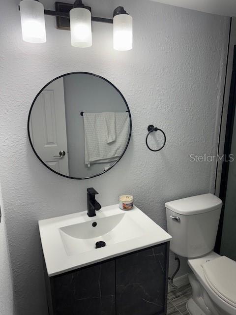 bathroom with toilet, vanity, and a textured wall