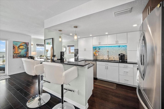 kitchen featuring stainless steel appliances, a sink, dark countertops, dark wood finished floors, and a textured ceiling