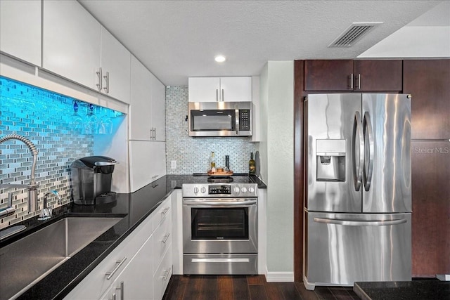 kitchen featuring appliances with stainless steel finishes, a sink, tasteful backsplash, dark wood-type flooring, and white cabinets