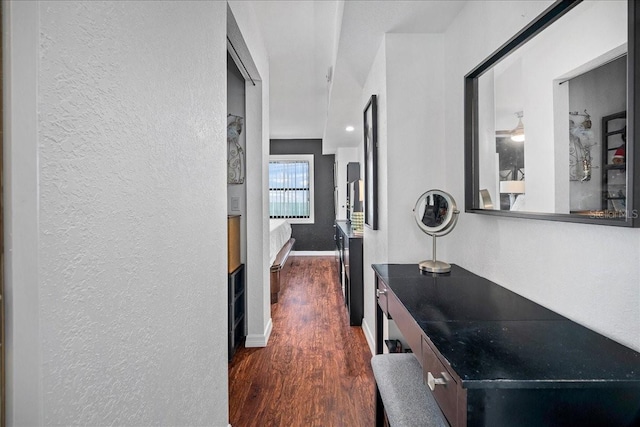 corridor featuring a textured wall, dark wood-style floors, and baseboards