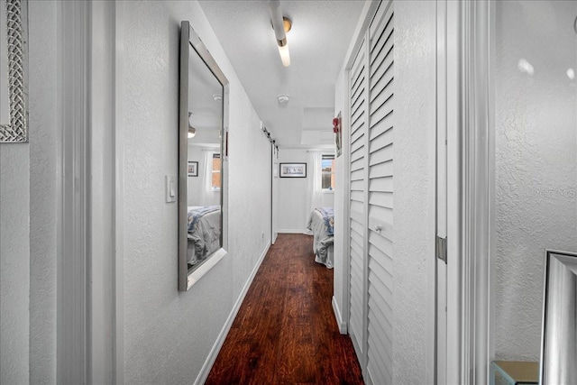 hall featuring a textured wall, wood finished floors, and baseboards