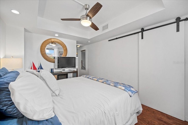 bedroom with a barn door, a raised ceiling, recessed lighting, wood finished floors, and a ceiling fan