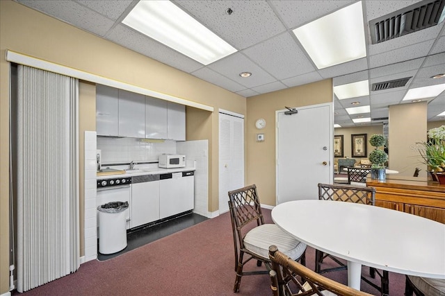 dining area with a drop ceiling, dark carpet, and baseboards