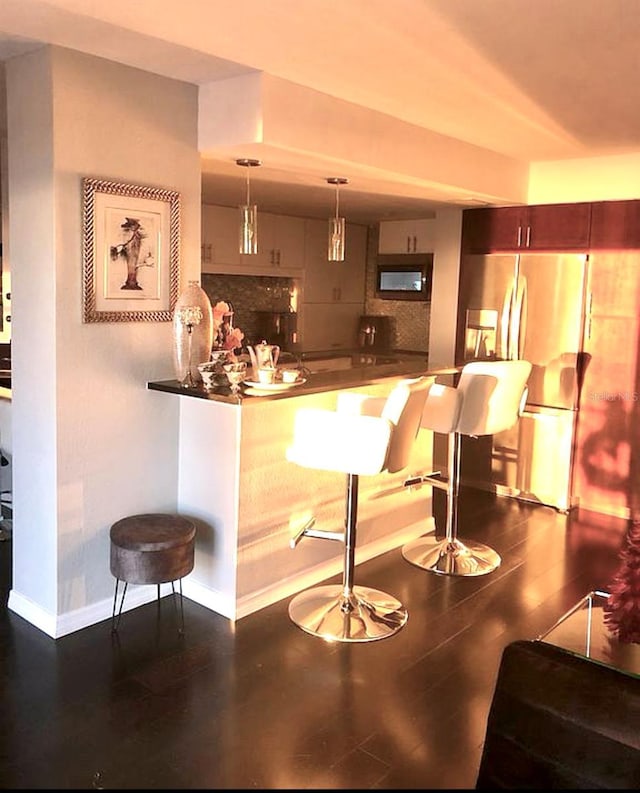 bar area featuring stainless steel fridge, black microwave, baseboards, dark wood-style flooring, and pendant lighting
