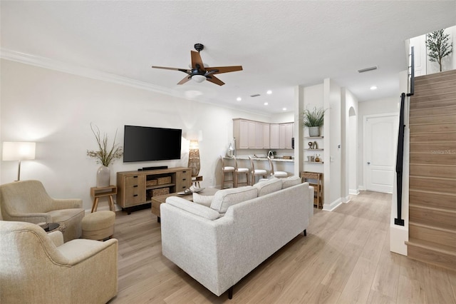 living area featuring ceiling fan, light wood-style floors, crown molding, recessed lighting, and arched walkways