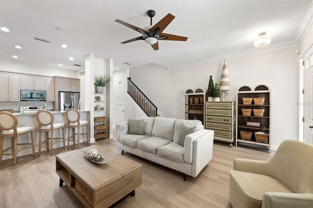 living room with recessed lighting, light wood-type flooring, a ceiling fan, ornamental molding, and stairs