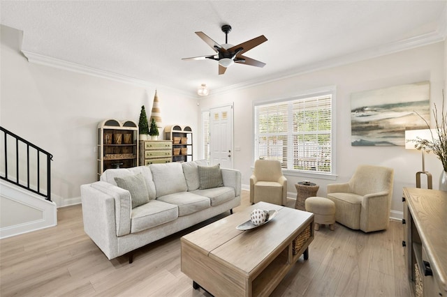 living room featuring ornamental molding, light wood finished floors, ceiling fan, stairs, and baseboards