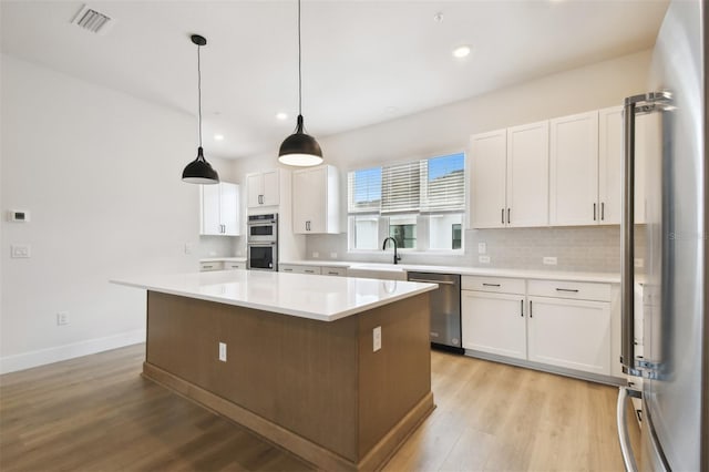 7240 Sutton Ln, Sarasota, FL 34240 - kitchen with stainless steel appliances, a sink, light wood-type flooring, white cabinets, and backsplash