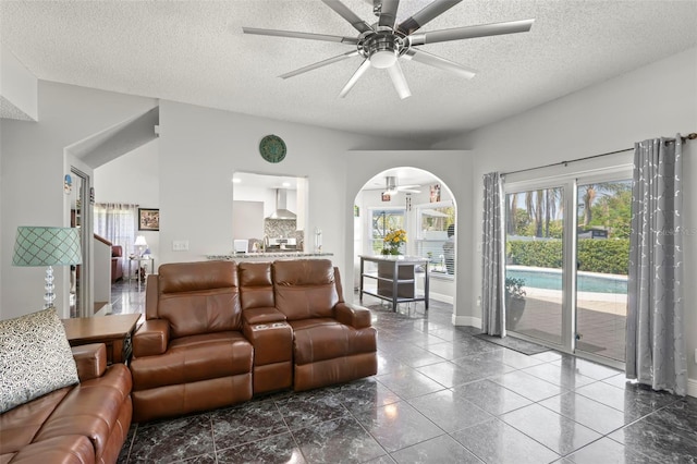 living area featuring a ceiling fan, a textured ceiling, baseboards, and arched walkways