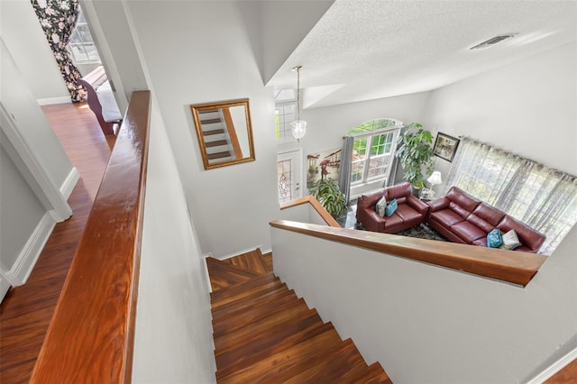 stairway with healthy amount of natural light, vaulted ceiling, wood finished floors, a textured ceiling, and baseboards