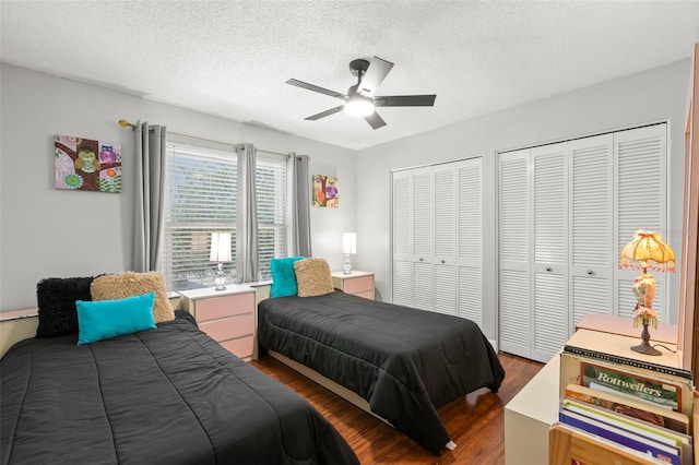 bedroom with multiple closets, dark wood-style flooring, a textured ceiling, and ceiling fan