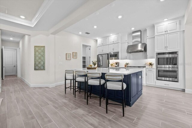 33750 Ocean Spray Ln, Wesley Chapel, FL 33543 - kitchen featuring wall chimney exhaust hood, stainless steel appliances, white cabinetry, a kitchen breakfast bar, and light countertops
