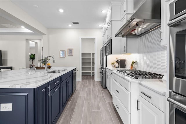33750 Ocean Spray Ln, Wesley Chapel, FL 33543 - kitchen with a sink, blue cabinetry, wall chimney range hood, appliances with stainless steel finishes, and a center island with sink
