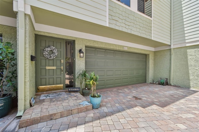 doorway to property featuring a garage, stucco siding, and decorative driveway