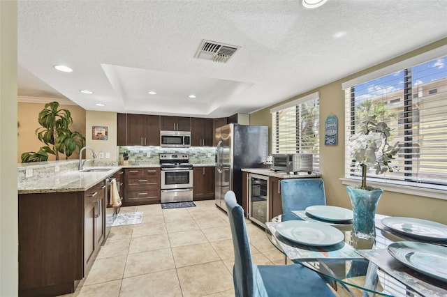 kitchen featuring stainless steel appliances, wine cooler, a raised ceiling, tasteful backsplash, and dark brown cabinetry