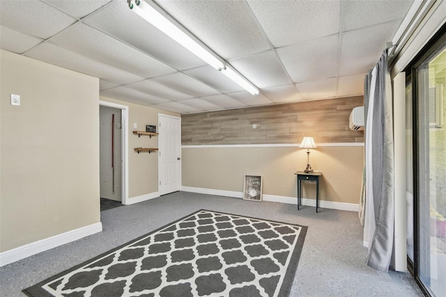 finished basement featuring a drop ceiling, baseboards, an AC wall unit, and wood walls