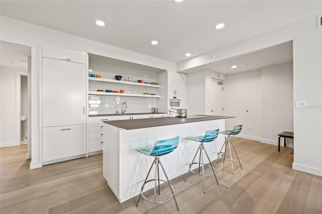 kitchen with dark countertops, open shelves, light wood finished floors, white cabinetry, and recessed lighting