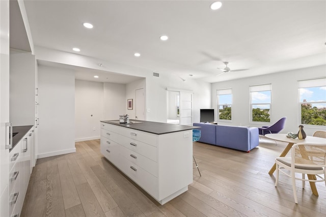 kitchen with dark countertops, a kitchen island, white cabinets, light wood-type flooring, and recessed lighting