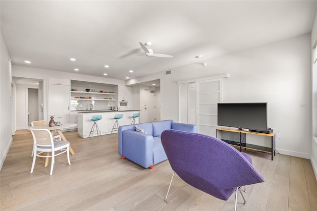 living area featuring recessed lighting, light wood-style floors, ceiling fan, bar, and baseboards