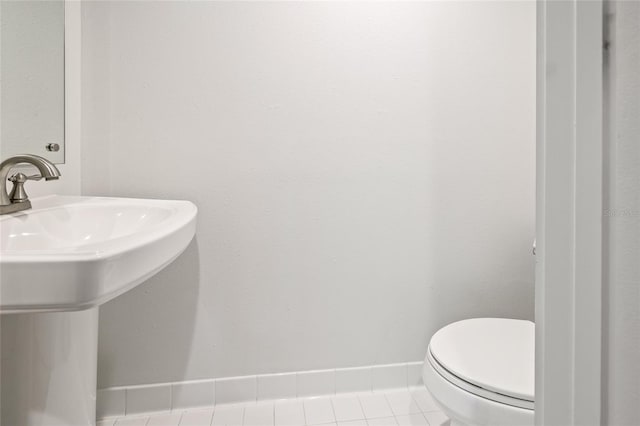 half bathroom with a sink, baseboards, toilet, and tile patterned flooring