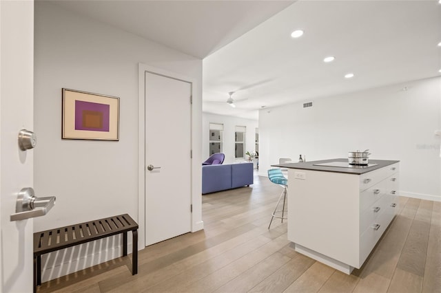 kitchen featuring white cabinetry, a kitchen breakfast bar, recessed lighting, dark countertops, and light wood-style flooring