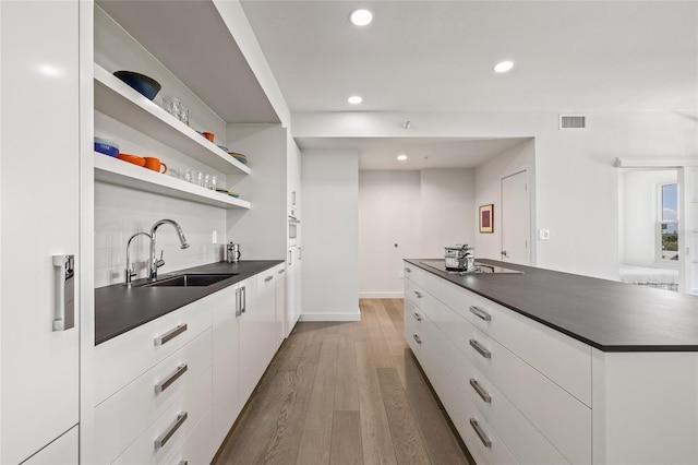 kitchen with dark countertops, a sink, modern cabinets, recessed lighting, and wood finished floors