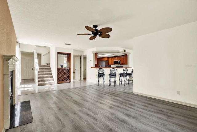 14561 El Paseo Dr, Seminole, FL 33776 - unfurnished living room with light wood finished floors, ceiling fan, a fireplace with flush hearth, and baseboards