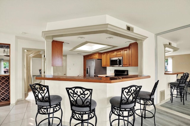 14561 El Paseo Dr, Seminole, FL 33776 - kitchen featuring stainless steel appliances, a breakfast bar area, brown cabinetry, and a peninsula