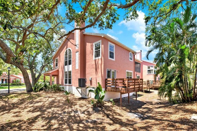 14561 El Paseo Dr, Seminole, FL 33776 - view of property exterior featuring stucco siding, a deck, cooling unit, and a chimney