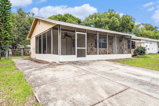 back of house featuring a sunroom, a gate, stucco siding, concrete driveway, and stone siding