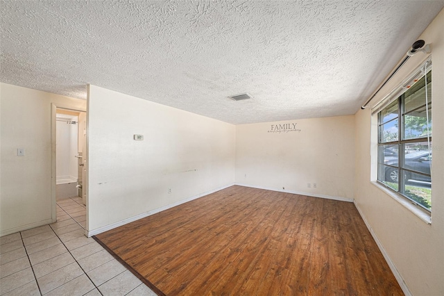 empty room with a textured ceiling, baseboards, and light wood-style flooring