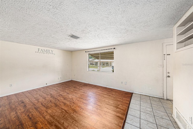 empty room with light wood-style flooring, a textured ceiling, and baseboards
