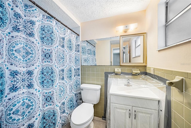 full bathroom featuring tile walls, a textured ceiling, toilet, vanity, and a wainscoted wall