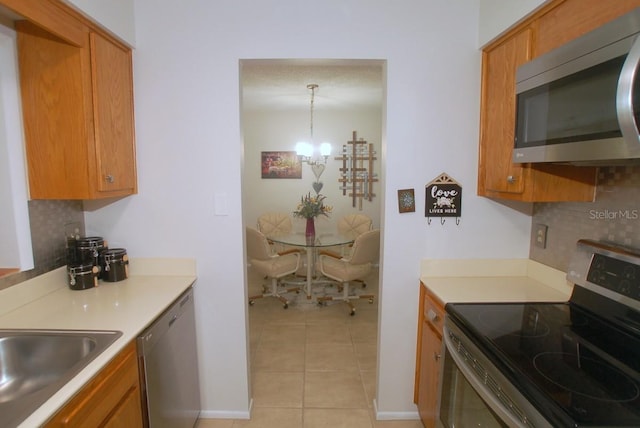 1126 Tarridon Ct, Dunedin, FL 34698 - kitchen with appliances with stainless steel finishes, tasteful backsplash, brown cabinetry, and a chandelier