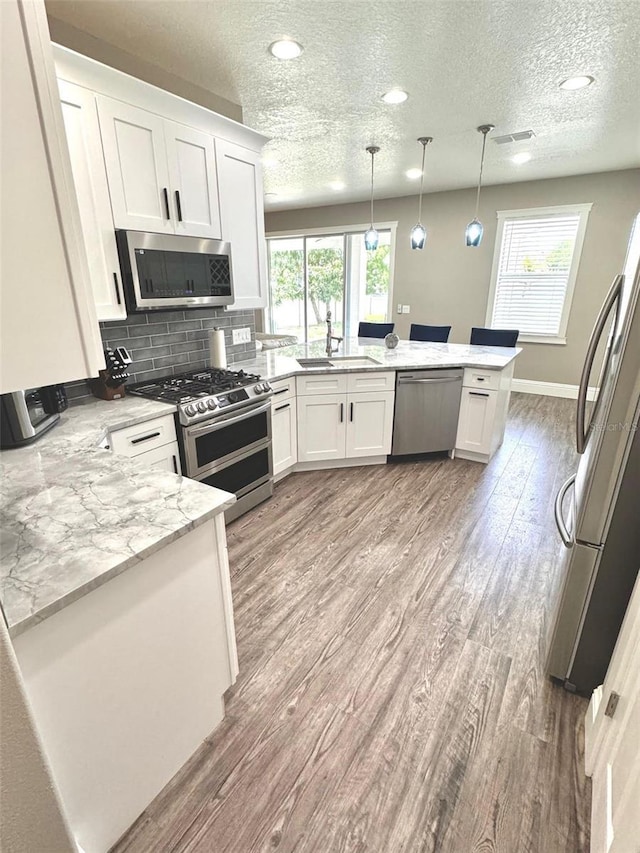 1147 Halapa Way, Trinity, FL 34655 - kitchen featuring appliances with stainless steel finishes, a peninsula, white cabinets, light wood-style flooring, and a textured ceiling
