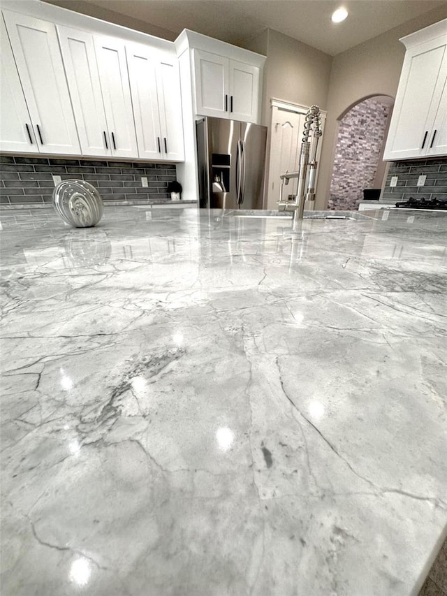 1147 Halapa Way, Trinity, FL 34655 - kitchen view of stainless steel fridge, decorative backsplash, light stone counters, arched walkways, and white cabinets