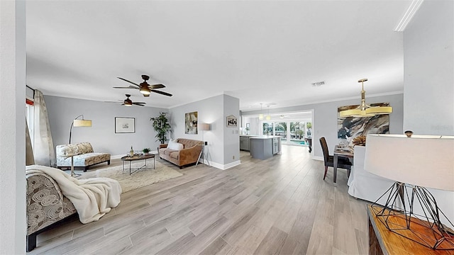 living area featuring light wood-type flooring, ceiling fan, ornamental molding, and baseboards