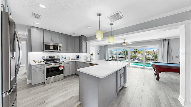 kitchen with stainless steel appliances, gray cabinets, a sink, a peninsula, and light wood-style floors