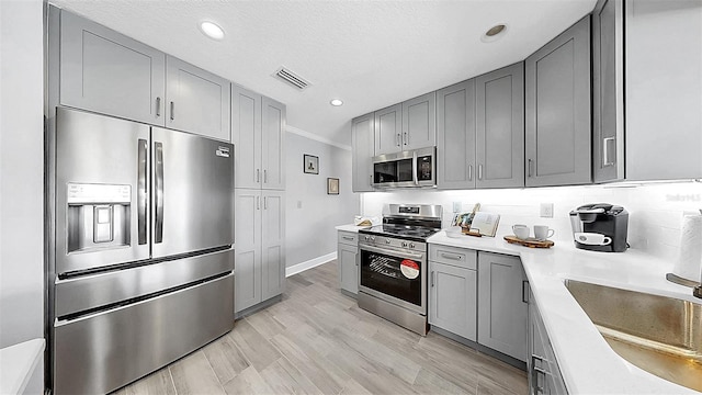 kitchen with stainless steel appliances, gray cabinetry, light countertops, crown molding, and a sink
