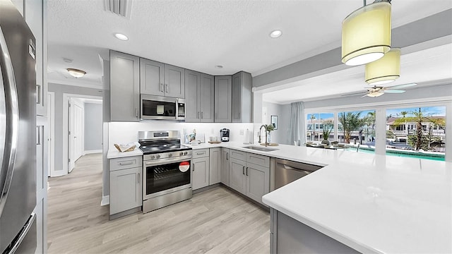 kitchen featuring gray cabinetry, stainless steel appliances, a sink, a ceiling fan, and light countertops