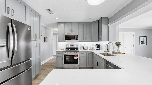 kitchen featuring appliances with stainless steel finishes, gray cabinetry, a sink, light wood-style floors, and ornamental molding