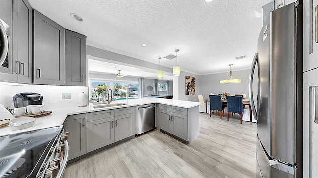 kitchen featuring appliances with stainless steel finishes, a sink, gray cabinetry, a peninsula, and light countertops