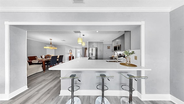 kitchen with appliances with stainless steel finishes, a kitchen breakfast bar, gray cabinets, light wood finished floors, and crown molding