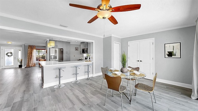 dining space featuring a ceiling fan, baseboards, light wood-type flooring, and crown molding