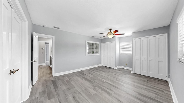 unfurnished bedroom featuring two closets, baseboards, light wood-type flooring, and ceiling fan