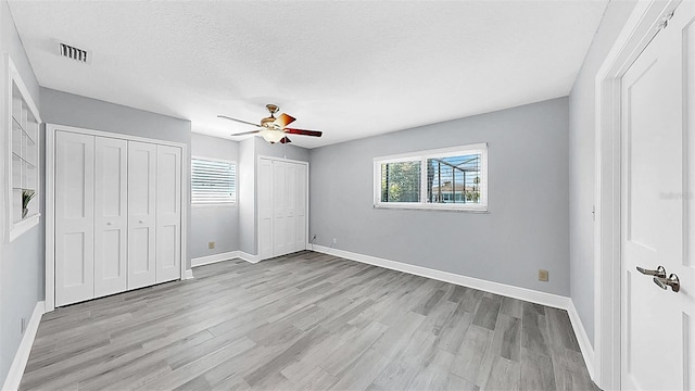 unfurnished bedroom with two closets, light wood finished floors, baseboards, ceiling fan, and a textured ceiling