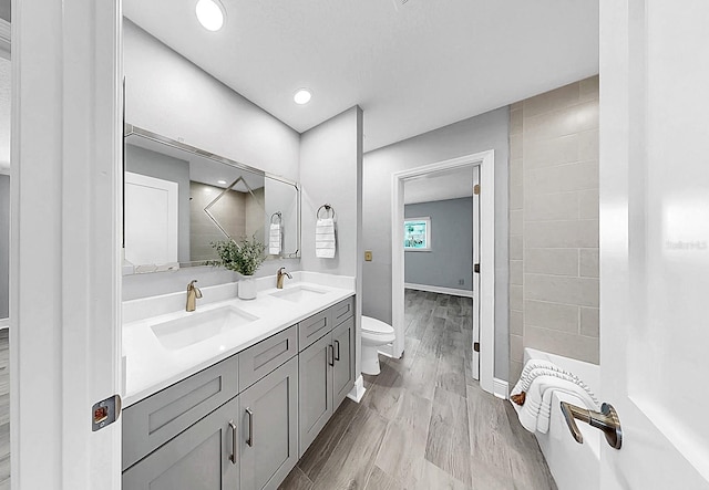 bathroom with toilet, double vanity, baseboards, and recessed lighting