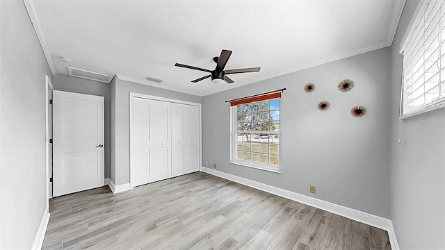 unfurnished bedroom with light wood-style flooring, baseboards, a closet, attic access, and ornamental molding