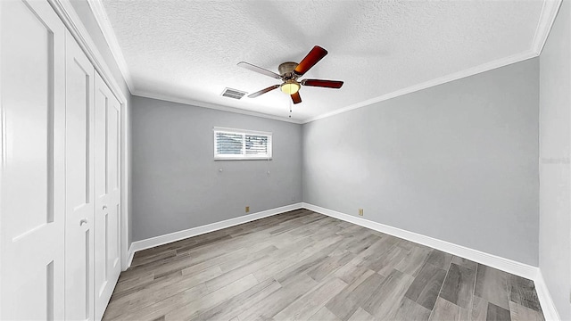 unfurnished bedroom featuring a closet, wood finished floors, a textured ceiling, crown molding, and baseboards