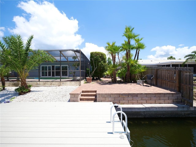 dock with a patio area, an outdoor pool, fence, and glass enclosure
